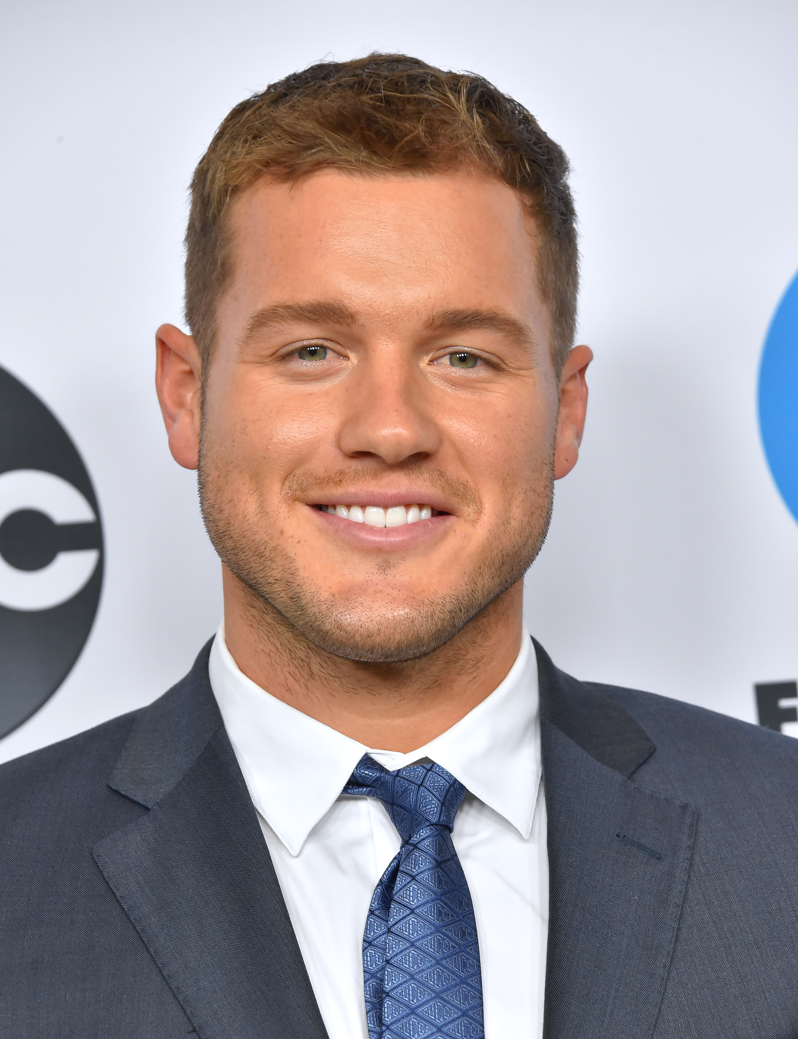 A photo showing Colton Underwood in a gray suit with a white inner T-shirt and blue tie.