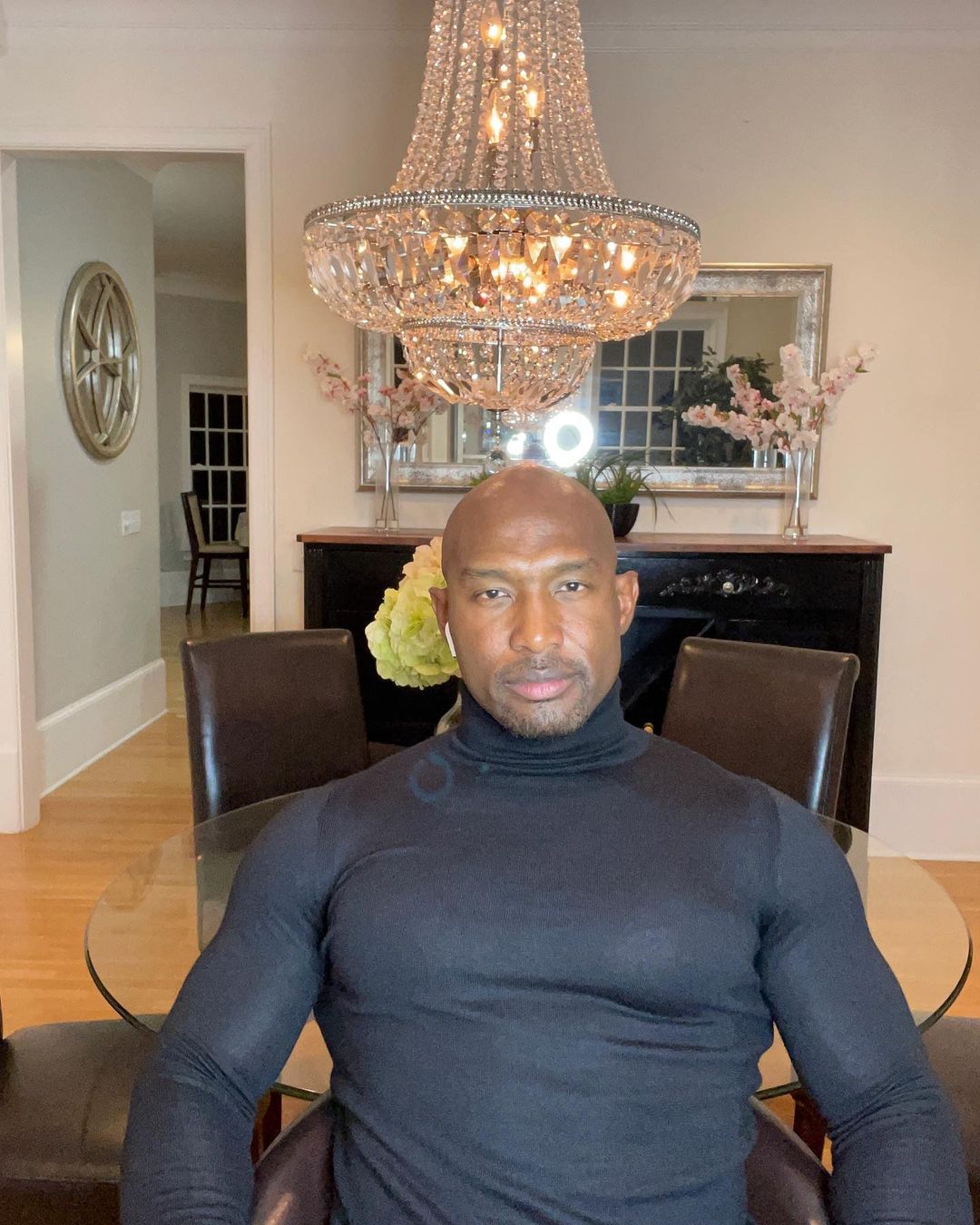 A photo showing Martell Holt sitting at his dining table in a black body-hug turtle-neck shirt.