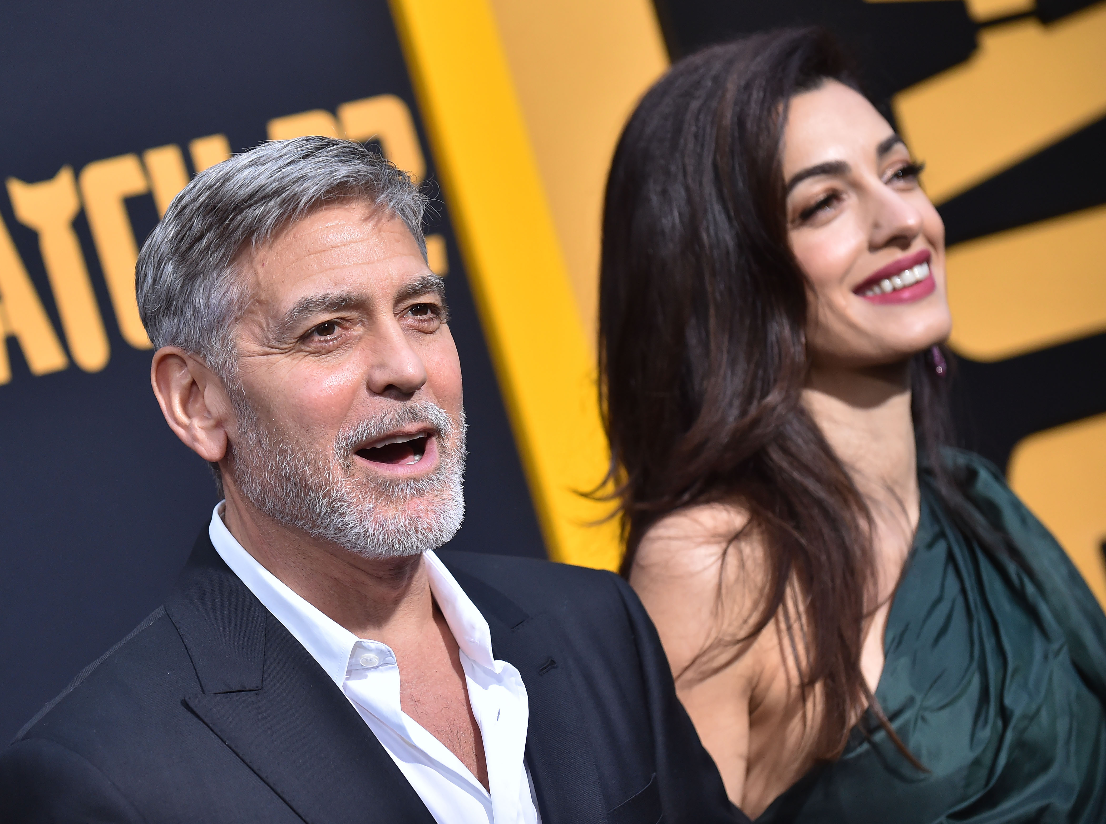 A photo of George Clooney and Amal Alamuddin smiling at the cameras together at an event.