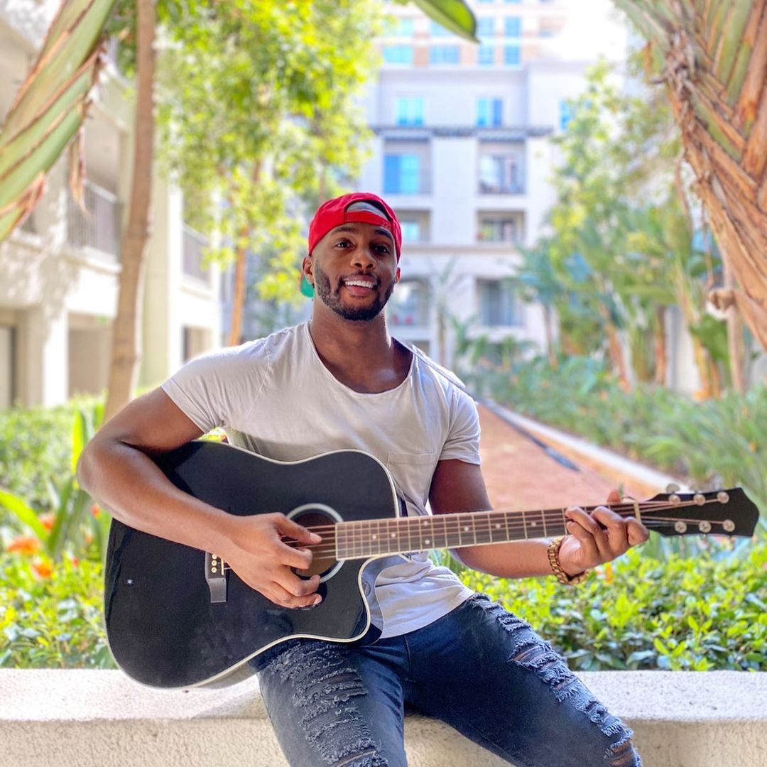 A phto of the handsome Uzoma Nwachukwu rocking a crazy jean and plain shirt, while holding a guitar.