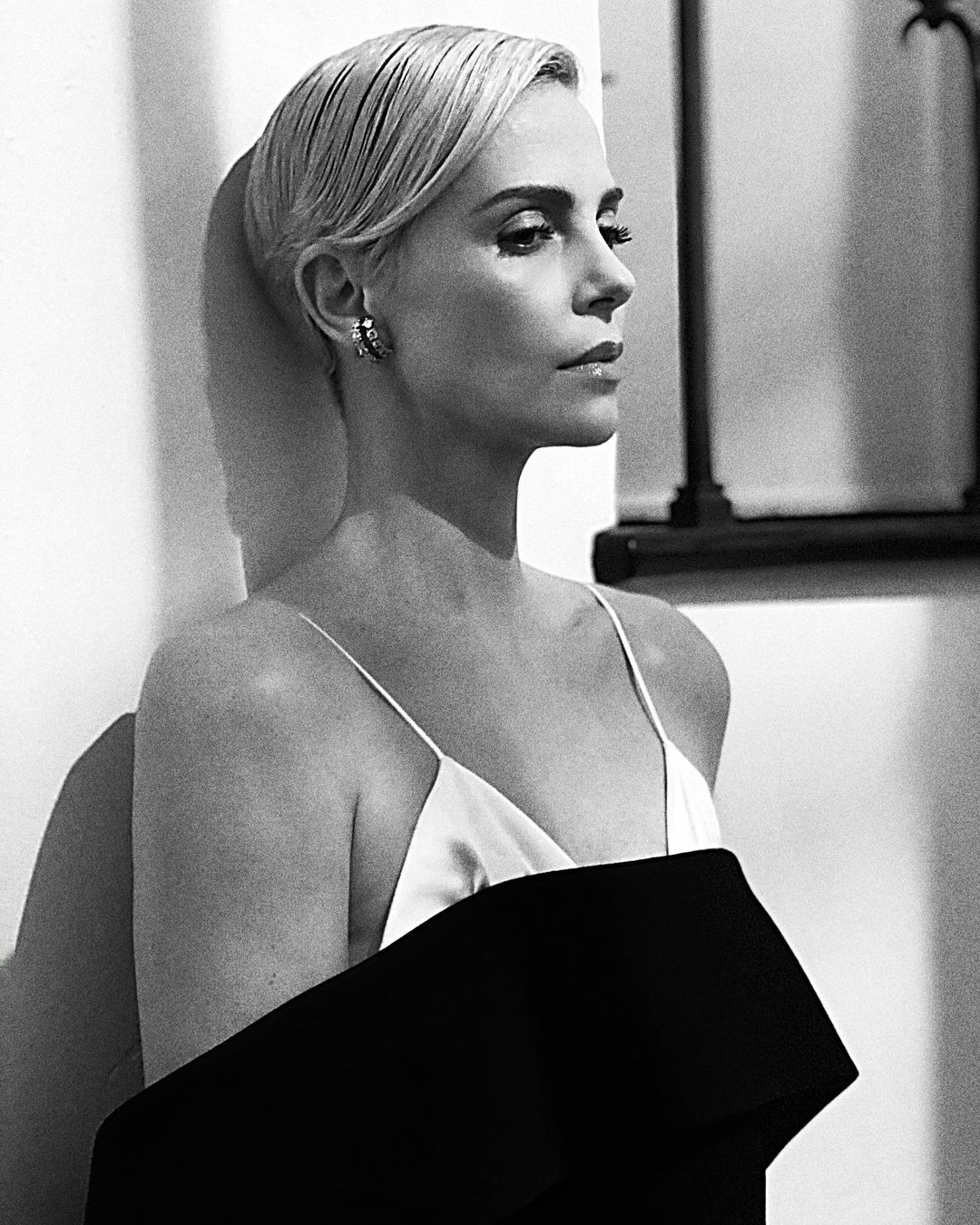 A photo showing Charlize Theron in a black off-shoulder outfit paired with a white sleeveless blouse and she looks amazing.