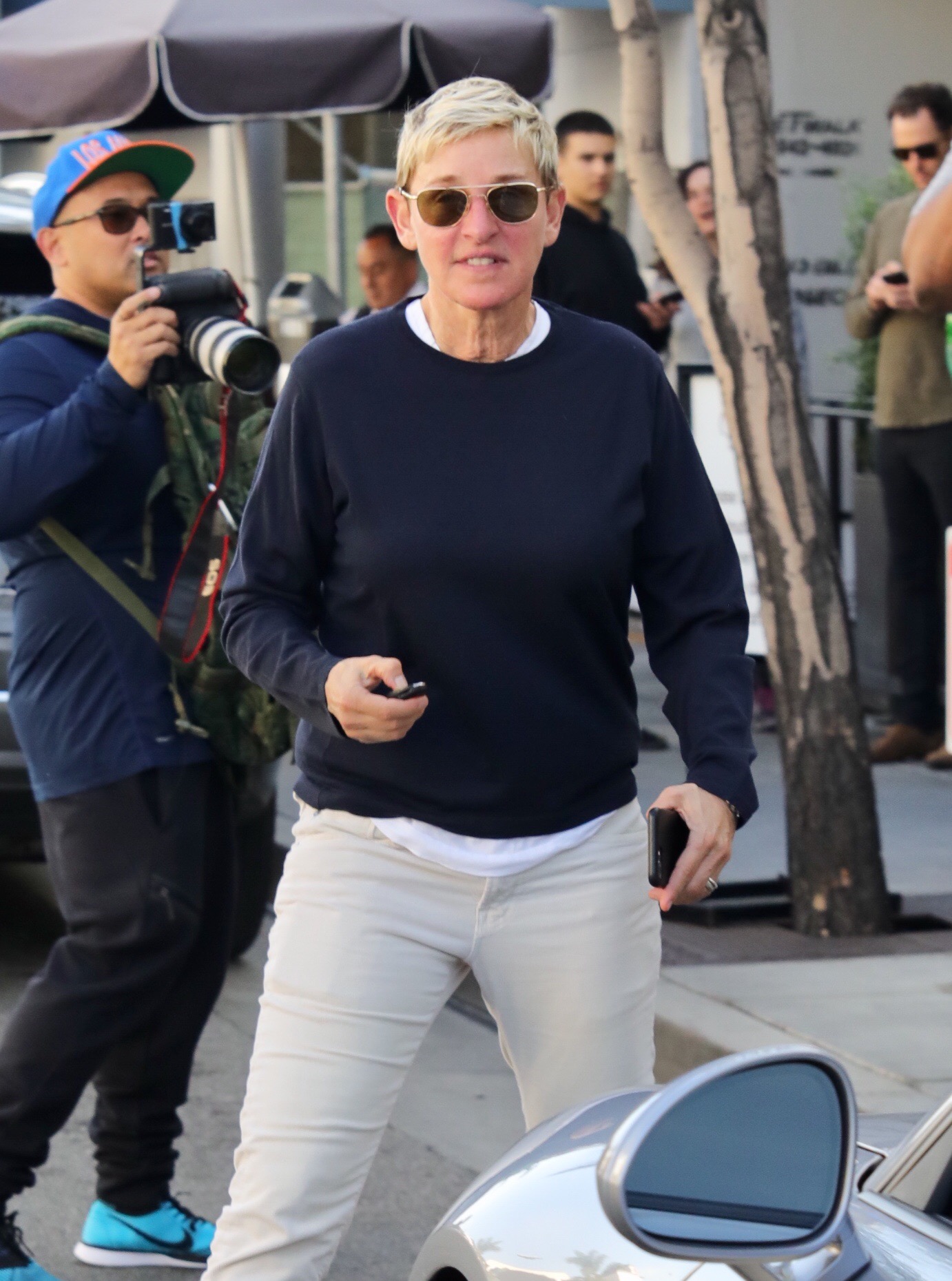 A photo of Ellen DeGeneres rocking a blue sweater on a white denim pant and black shades to match.