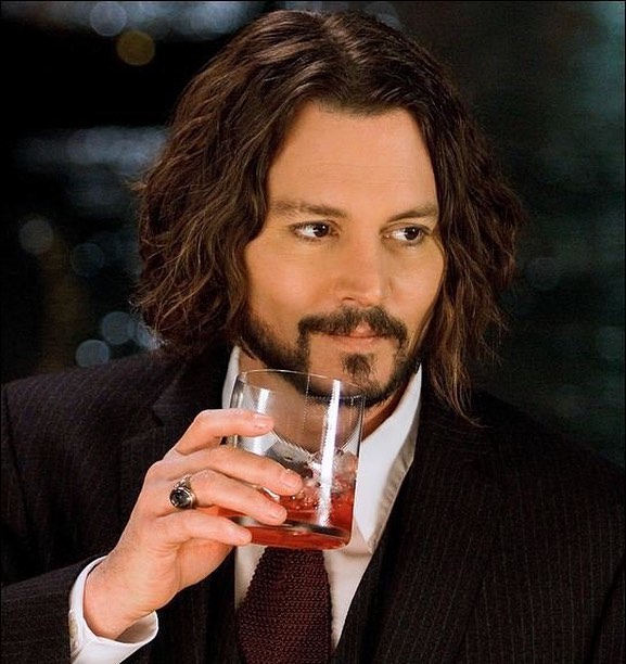 A photo showing Johnny Depp in a striped black suit, holding a glass with a red drink inside it.