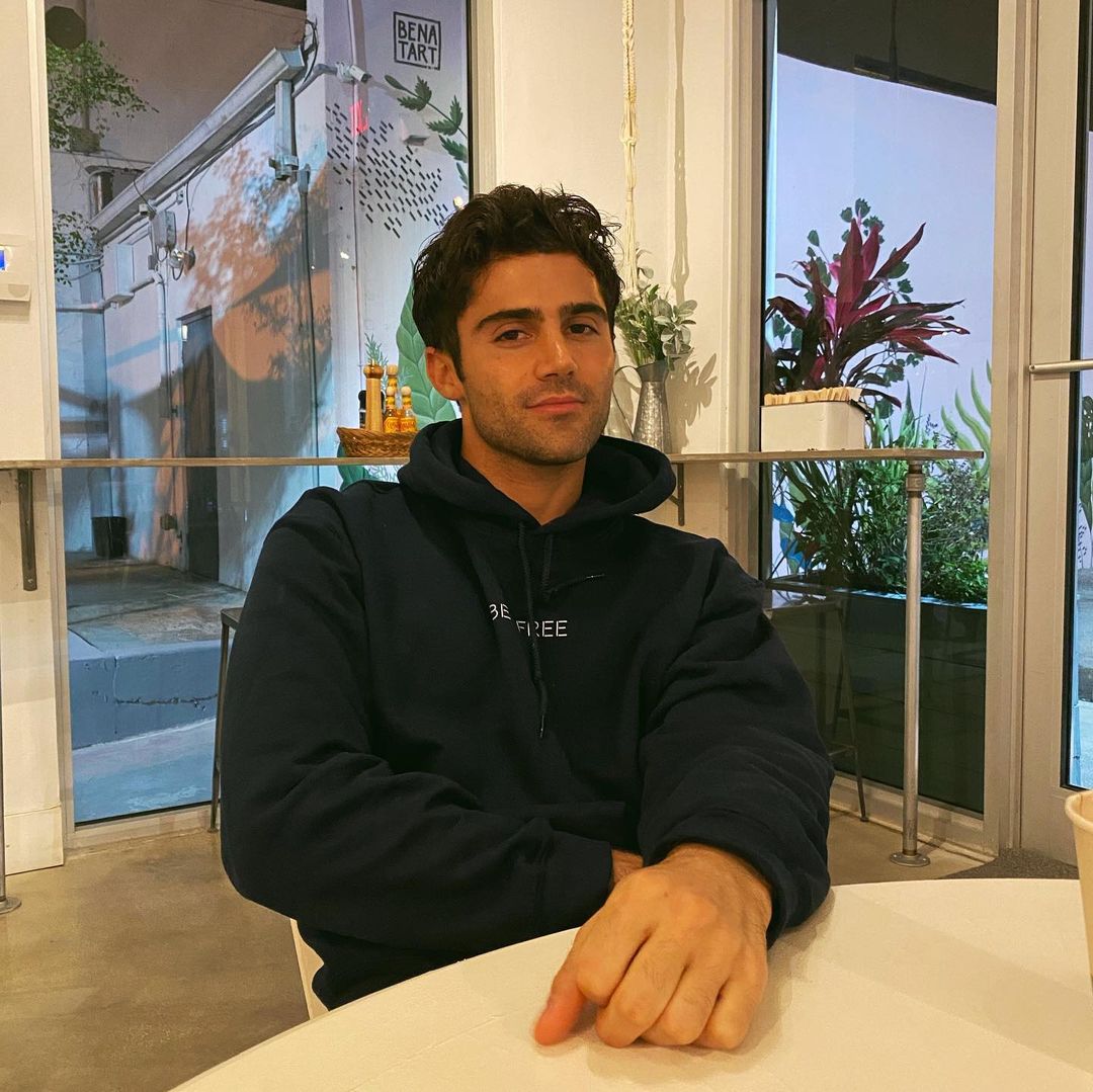 A photo of Max Ehrich sitting at a round table, in a black hoodie.