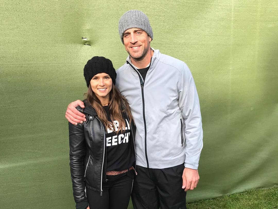 A throwback photo of Aaron Rodgers and Danica Patrick in casual clothes and beanies at an event.