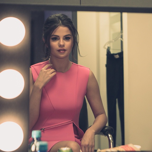 A picture of Selena Gomez rocking a pink dress, while sitting in front of a mirror.