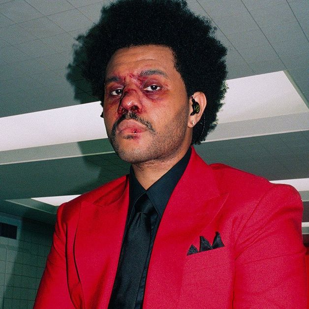 The Weeknd wears a red suit and an earpiece as he looks into the camera with a bloody nose and swollen red eyes.