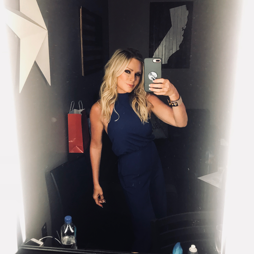 A photo of Tamra Judge wearing a blue jumpsuit in front of a mirror with a beautiful pose.