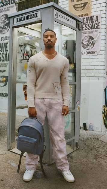 A photo of Michael B. Jordan sporting a striped pant and sweater, while holding a backpack.