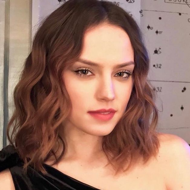 Daisy Ridley stares into the camera with wavy brown hair.