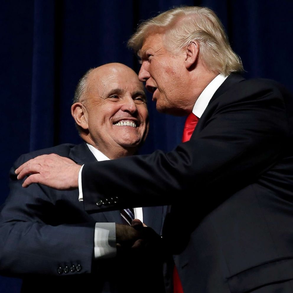 A photo showing President Donald Trump and Rudy Giuliani shaking hands and about to hug at an event.