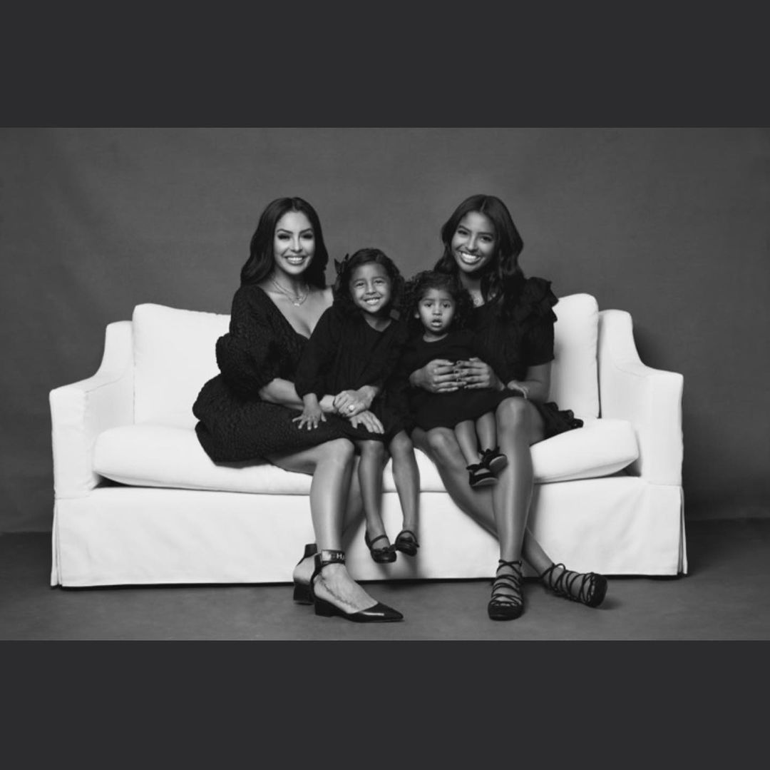 A photo showing Vanessa Bryant and her three beautiful daughters in balck dresses, seated on a white sofa.