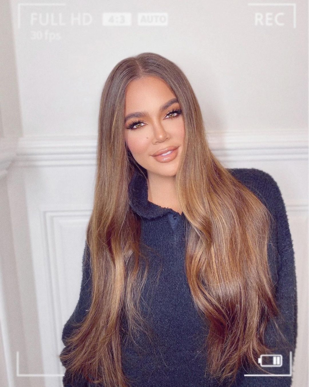 A photo showing Khloé Kardashian in a blue sweater and she has an incredible smile on her face.