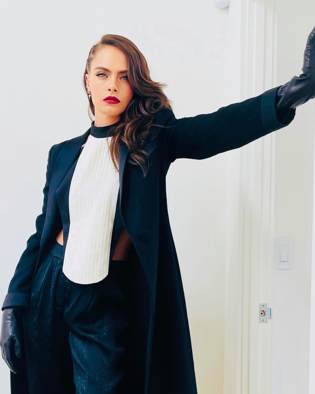 A photo showing Cara Delevingne in a blue three-piece outfit, posing beside a white wall.