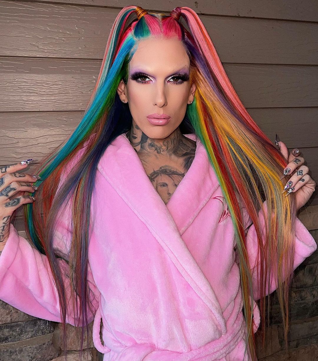 A lovely photo showi ng Jeffree Star in a pink robe his multicolored hair is perfectly styled into little ponytails in front.