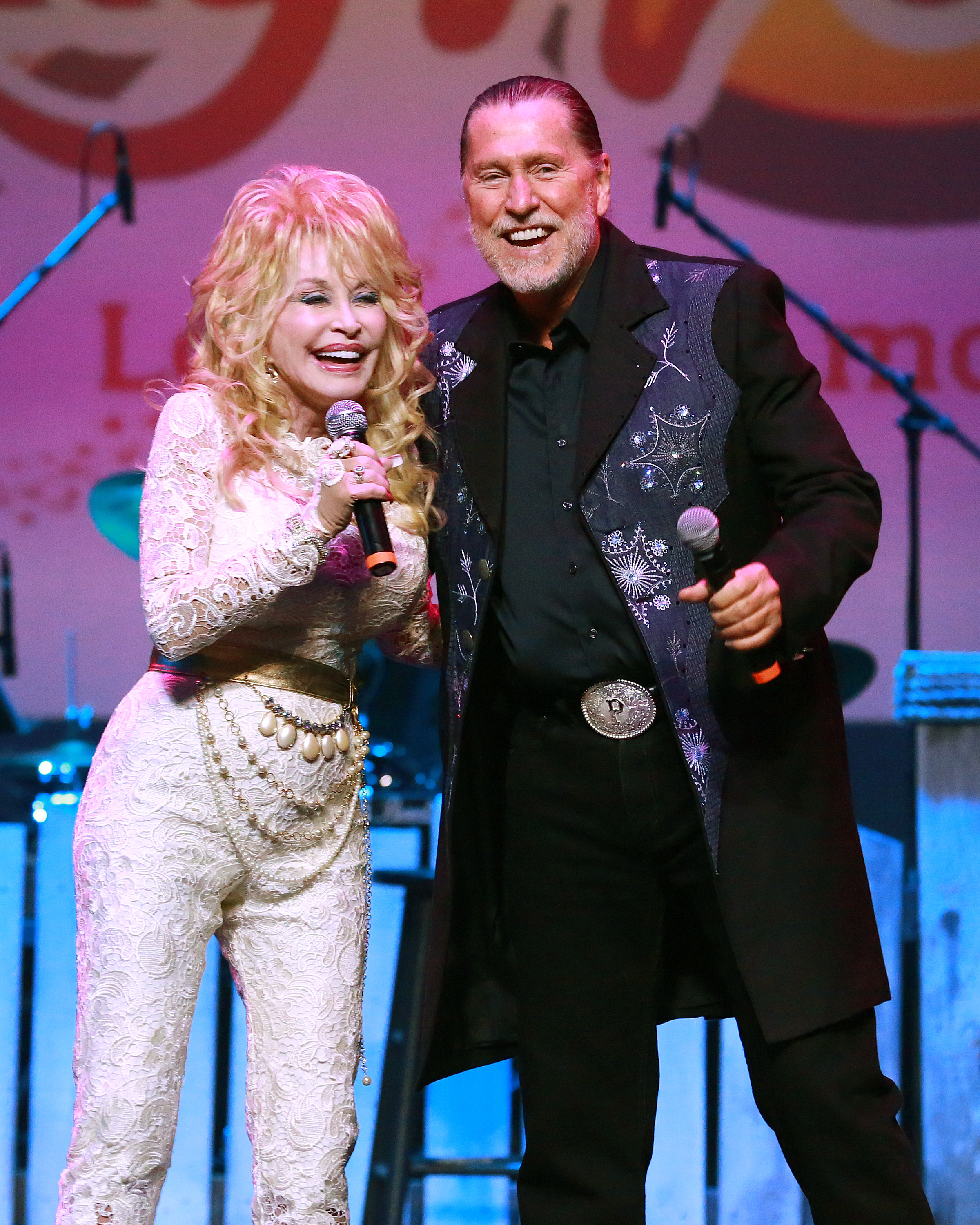 A picture of Dolly and Randy Parton singing together on stage with beautiful smiles on their faces.