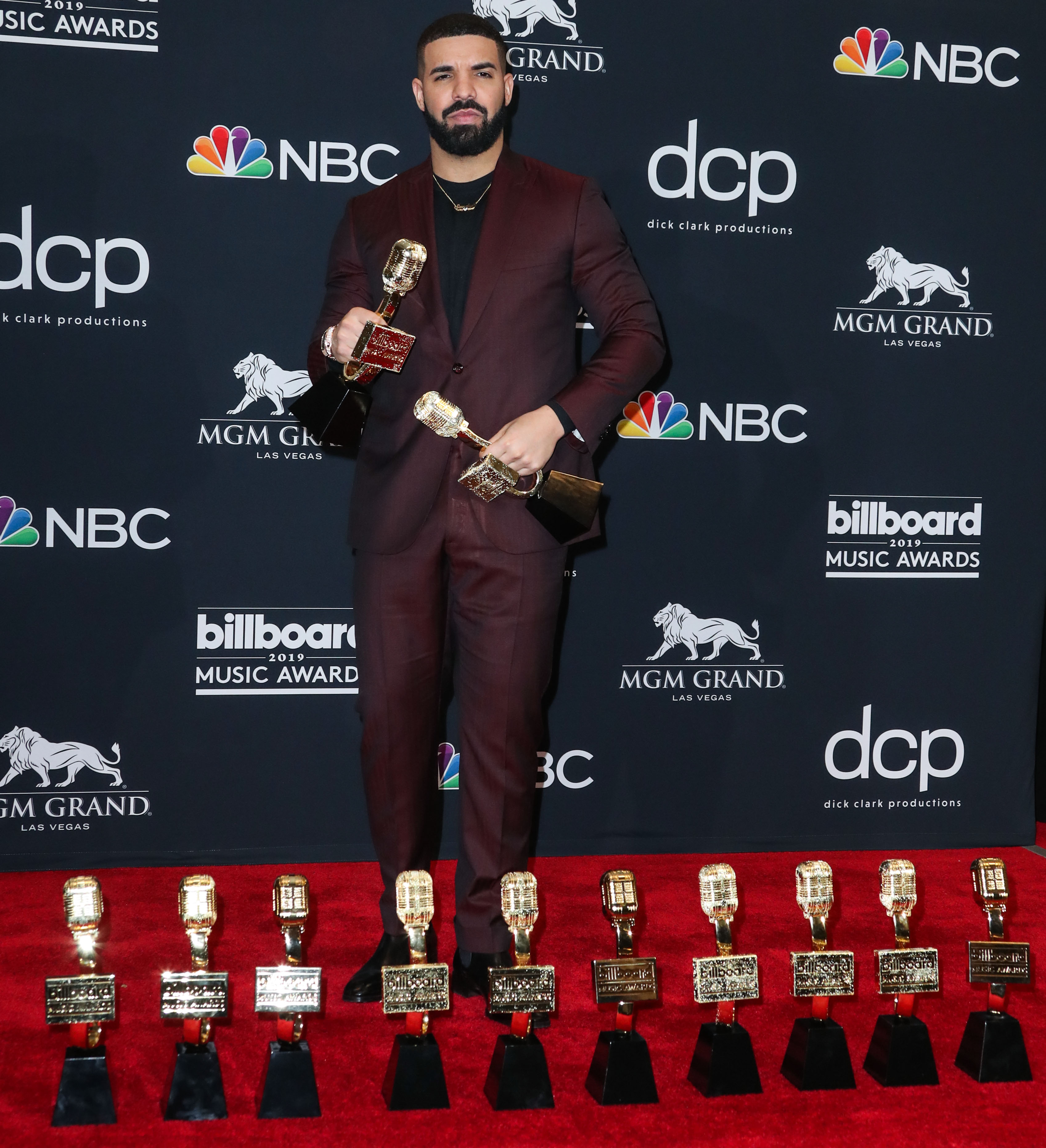 A photo showing Drake in a wine color suit and pant, photographed on the red carpet with his nemerous awards and he looks amazing.