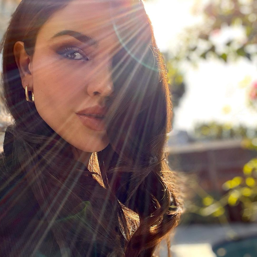 A selfie showing Eiza González outdoors, with the rays of sunlight shining on her face, that's partly covered with her hair.