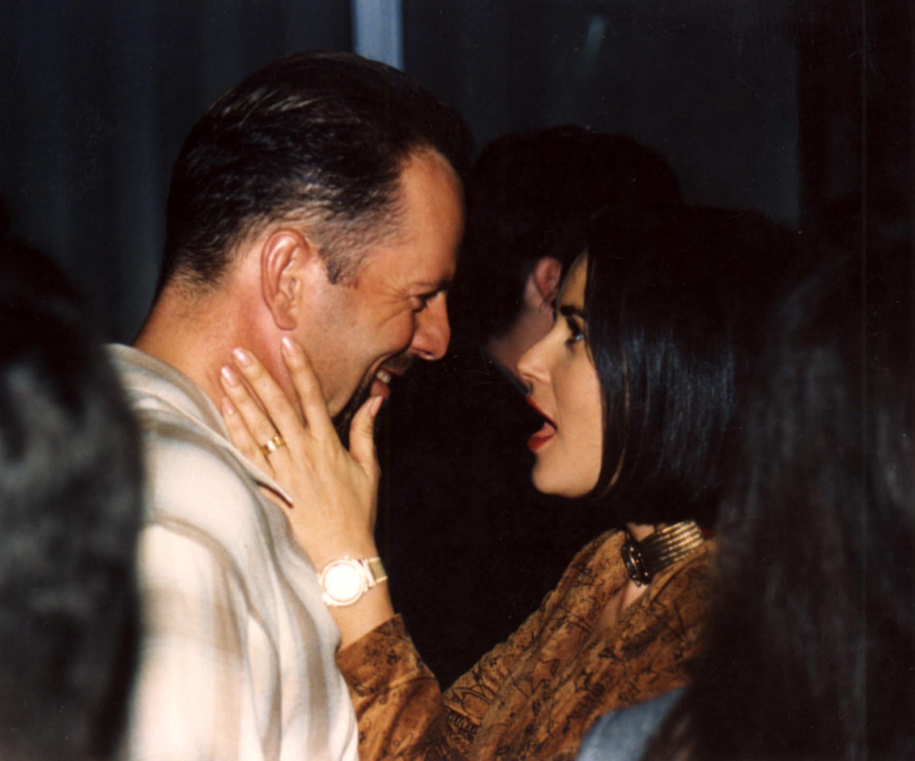 A photo showing Demi Moore holding Bruce Willis' face in her palms in the midst of people