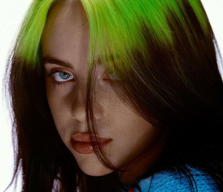 A close-up of Billie Eilish's face, showing off her dark hair and long lime-green roots.