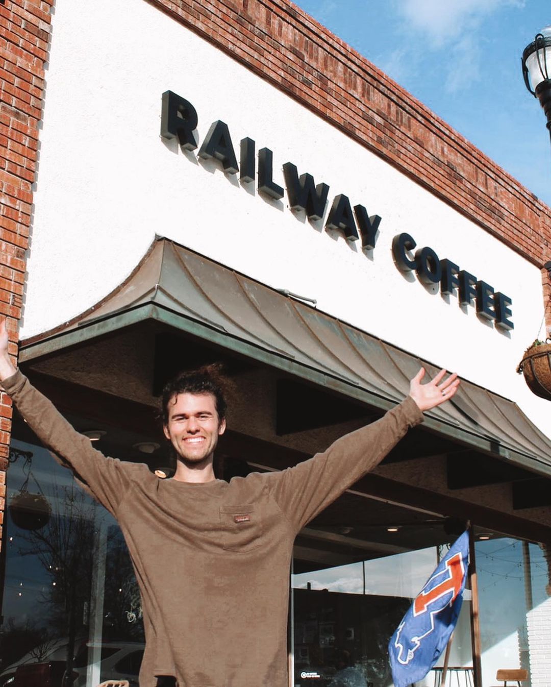 A photo shoeing John Luke with arms high in the sky and a bright smile at one of the railway coffee locations.