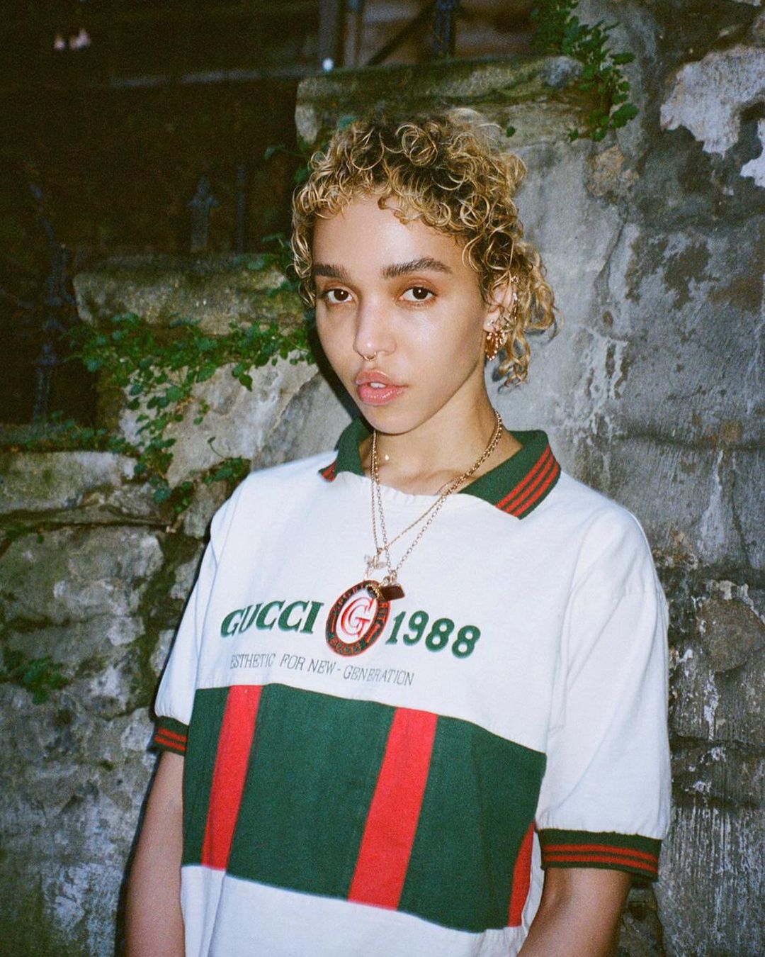 An amazing photo showing FKA Twigs rocking a gucci design polo shirt and gold necklaces around her neck.