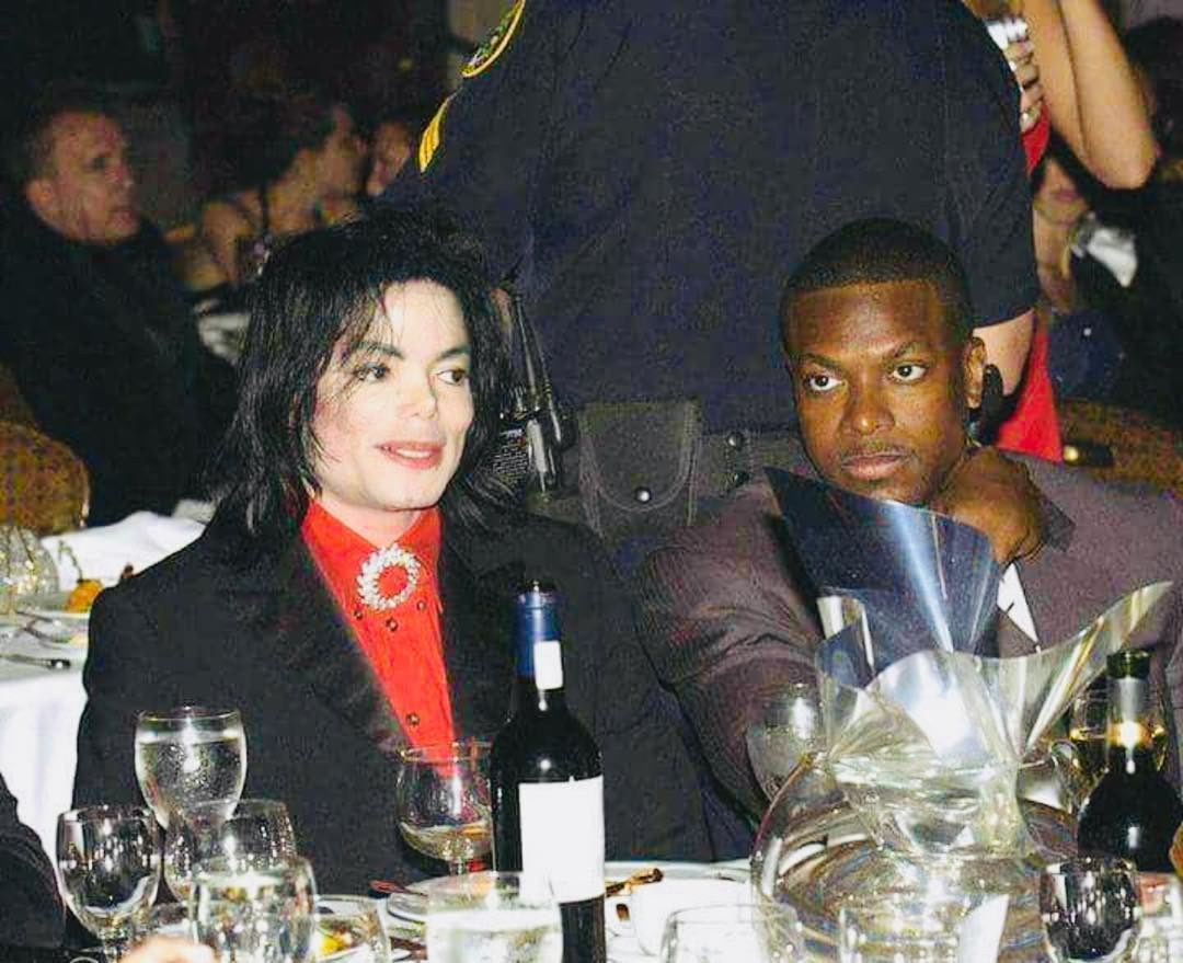 A throwback photo showing Chris Tucker and Michael Jackson at a diner table filled with bottles of wine and wine glasses.