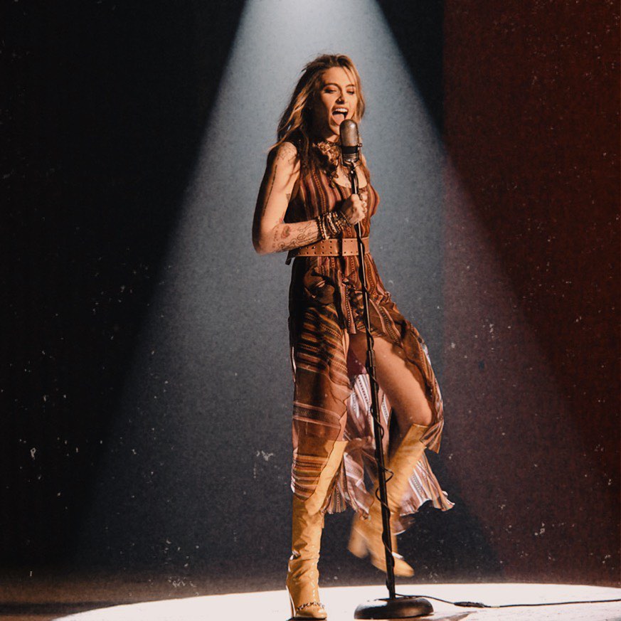 A photo of Paris Jackson in stage in a brown dress and knee-high boots.