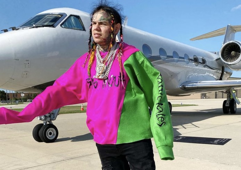 6ix9ine in front of his privetjet in his Tattle Tales apparel