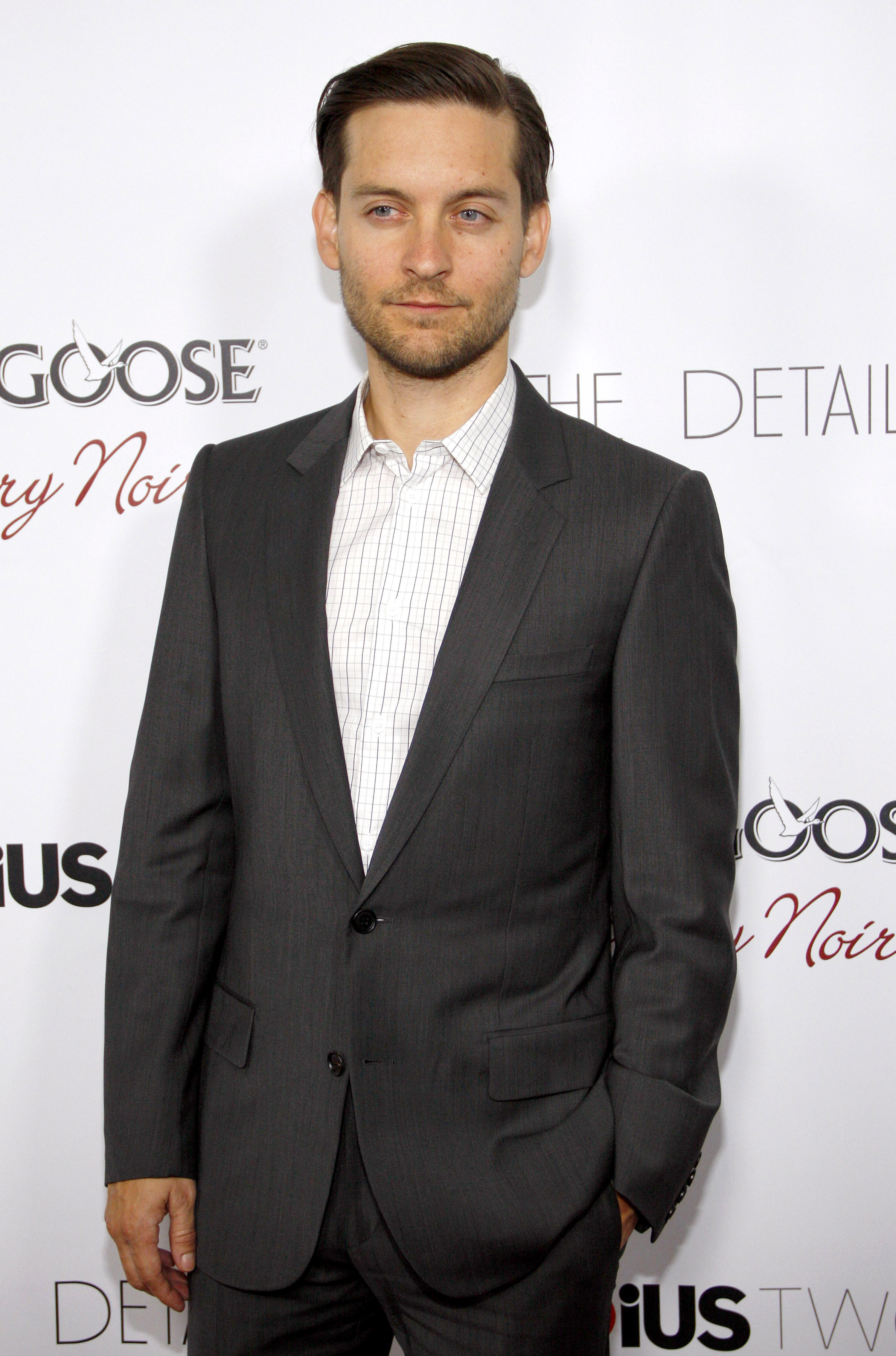 A photo of Tobey Maguire in a gray suit and pant, mixed with an inner striped T-shirt.