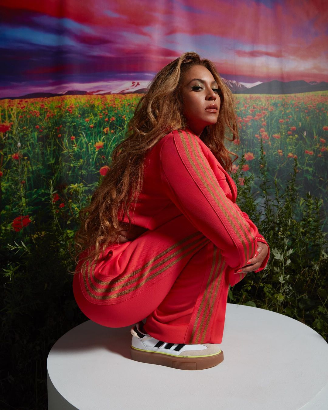 A stunning picture of Beyoncé wearing a pink colored outfit, crouched on a white table. 