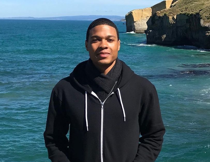 Ray Fisher wears a black hoodie as he stands in front of the ocean.