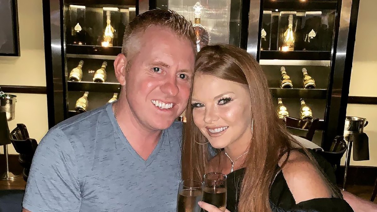 Brandi Redmond smiles with Bryan in front of a wine fridge.