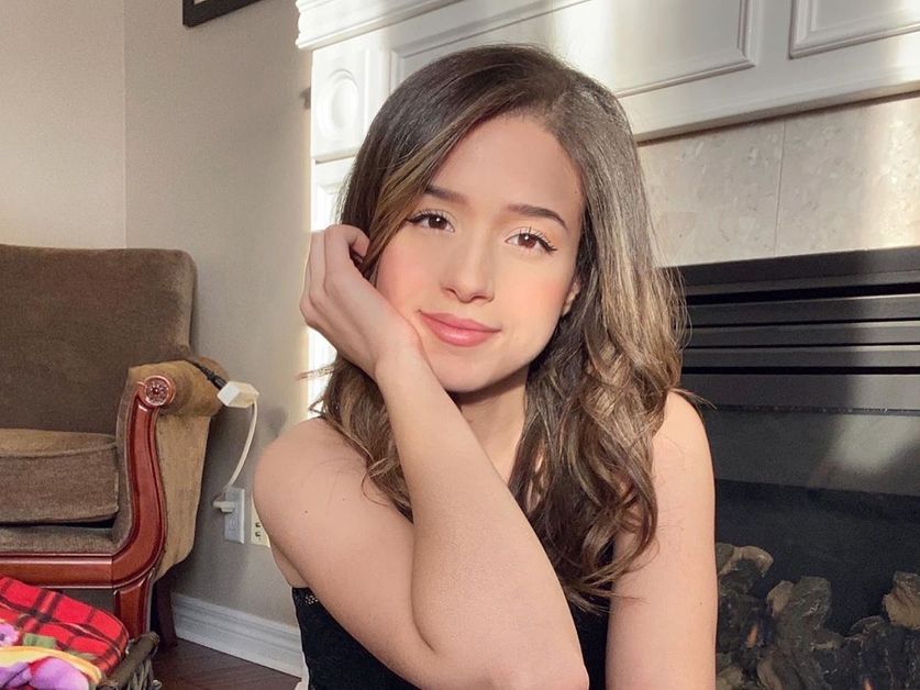 Pokimane poses in front of a fireplace