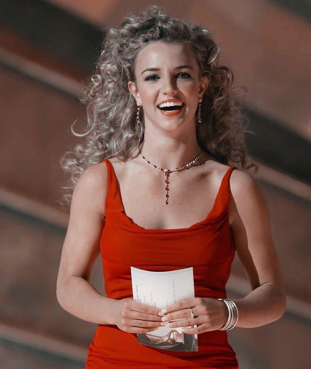 A throwback photo of Britney Spears in a red dress and matching jewellery set, holding a paper in her hands. 