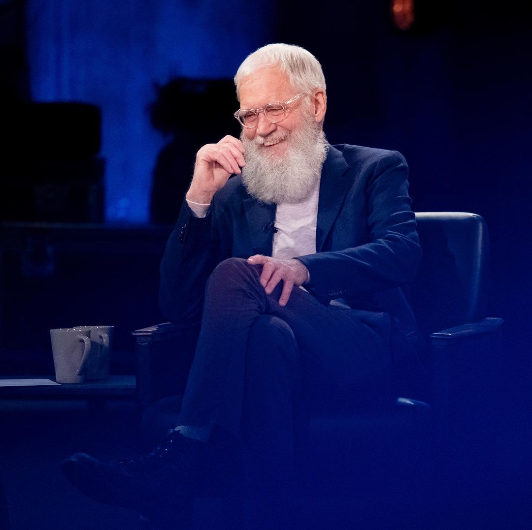 A photo showing David Letterman laughing hysterically while sitting, with two cups beside him.