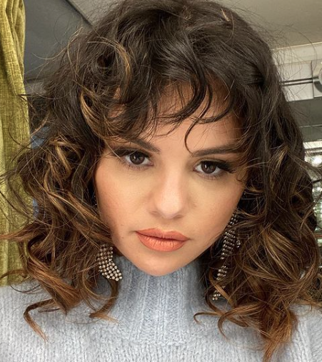Selena Gomez sports curly hair and a gray sweater.