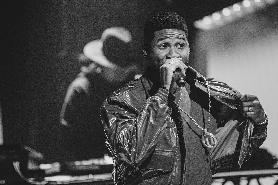 A black and white themed photo showing a Usher smiling during a performance. 