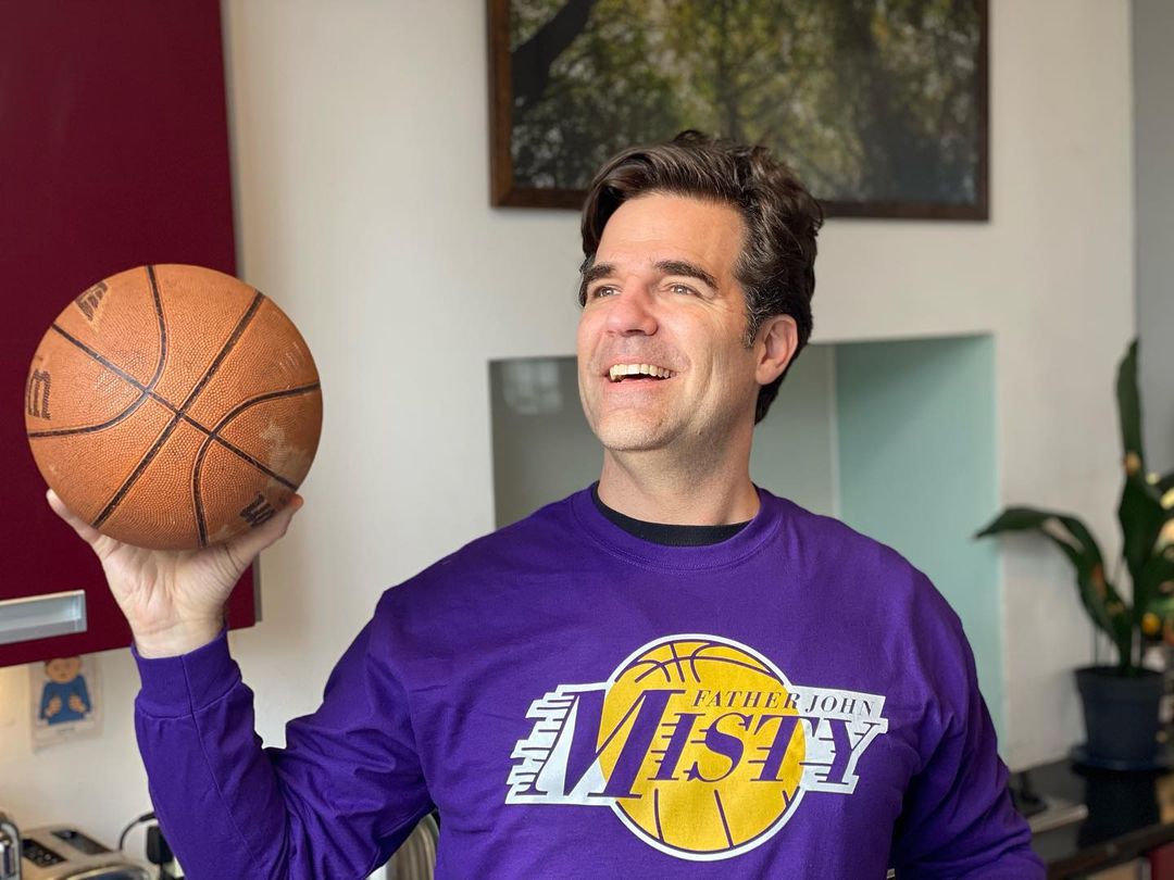 A photo of Rob Delaney in sweatshirt, holding a basketball in his right hand with an adorable smile on his face.