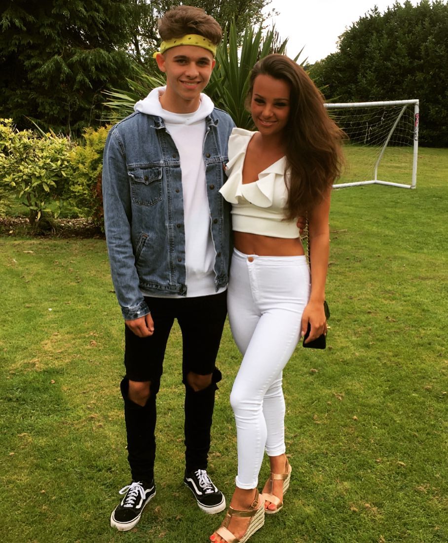 A pretty picture of Joe Warren-Plant and Nichole Hadlow, here Warren-Plant rocks a jean jacket with an inner white T-shirt, ripped jeans,sneakers and a band on his head, while Hadlow is wearind a pretty cream crop top with white pants and wedge shoes and hanging from her shoulder is a black purse.