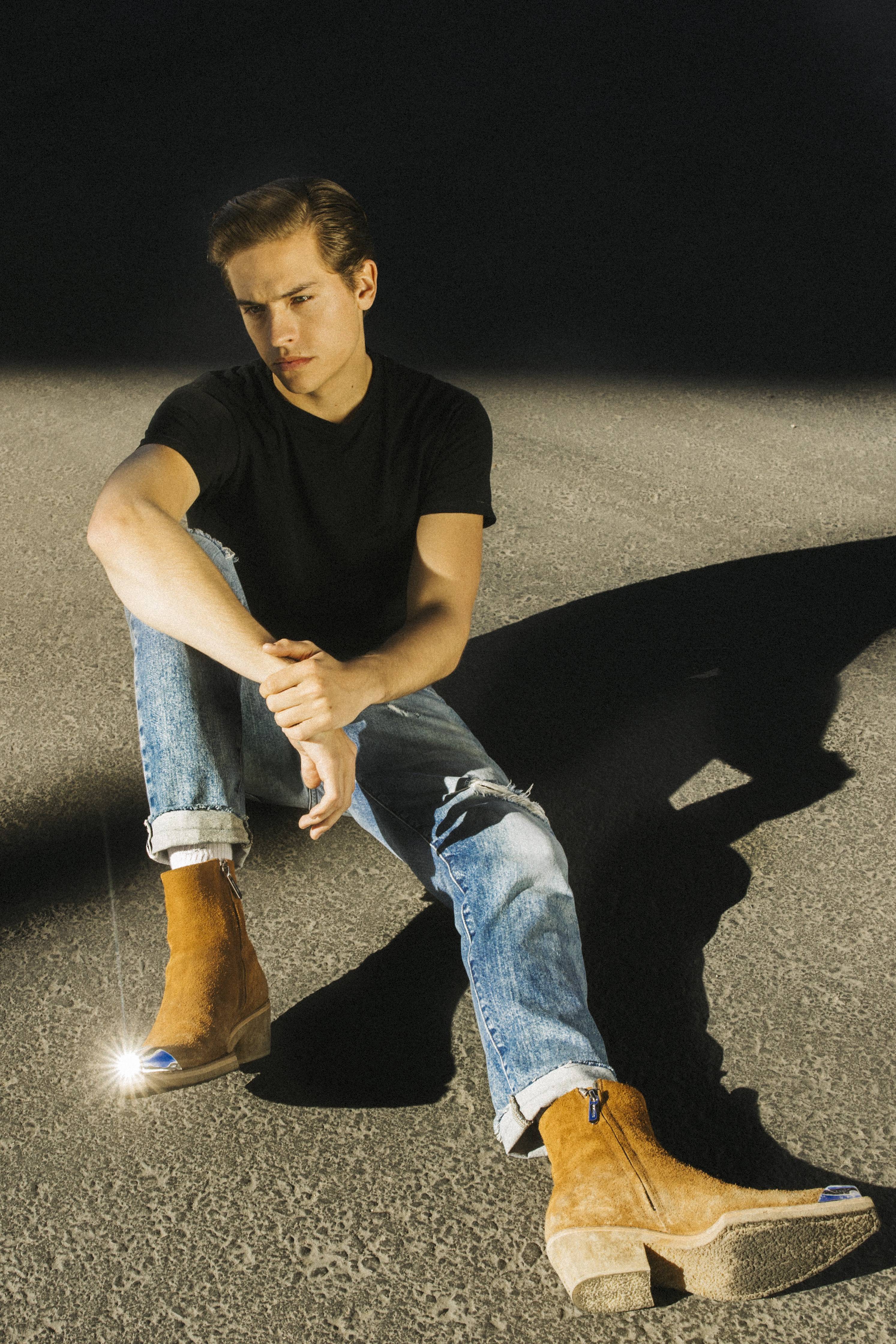 Dylan Sprouse looking handsome in a black shirt and denim jeans with brown shoes to match.