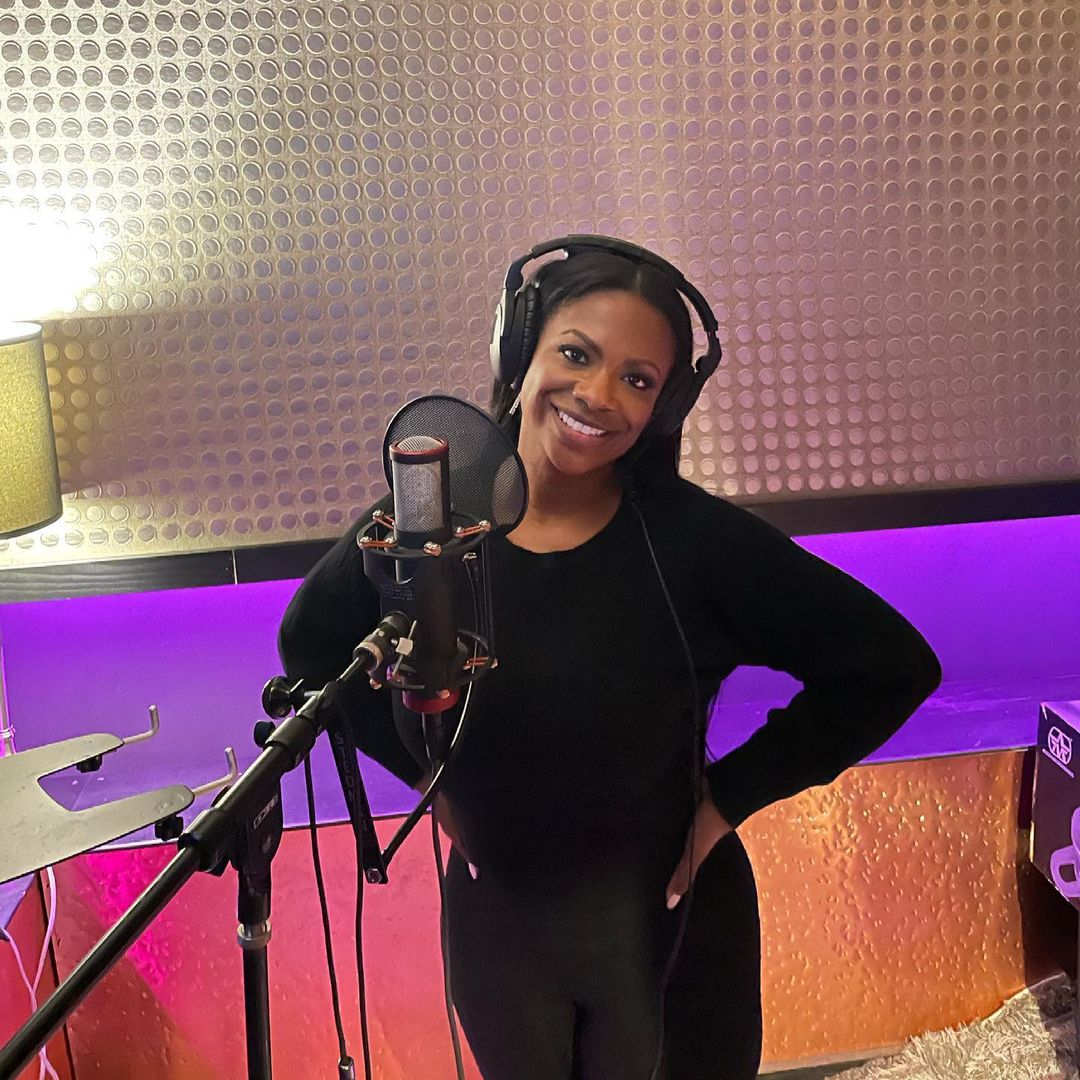 Kandi Burruss looks amazing in this black outfit with a headphone on her head in front of a microphone.