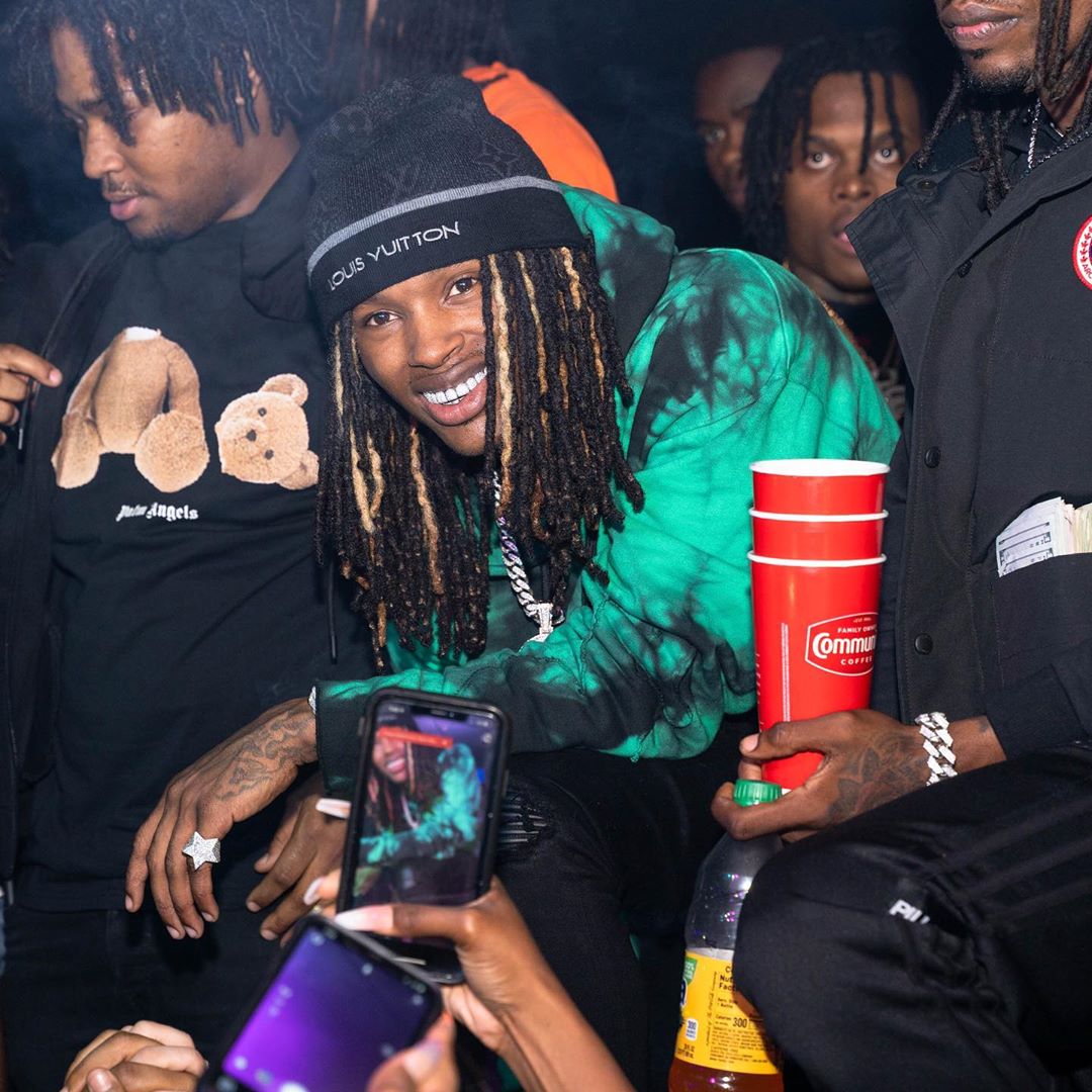 King Von looks incredible in this photo showing him among friends and he has on a green and black patterned hoodie with a louis vuitton cap.