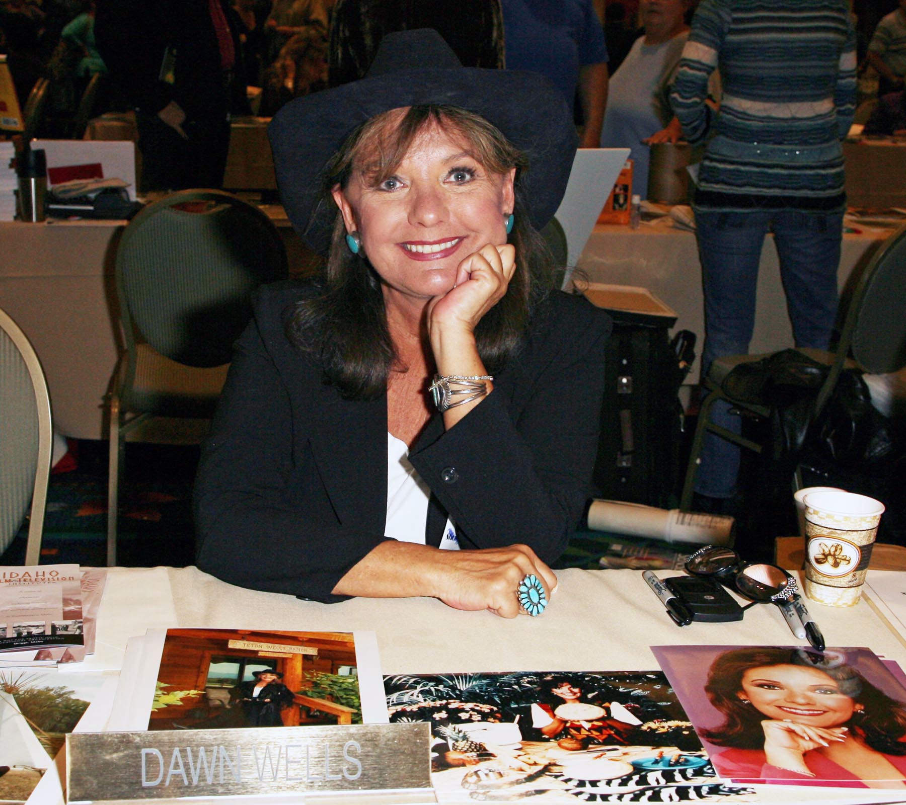 A photo of Dawn Wells sitting pretty in front of a table plastered with pictures of her in different locations.