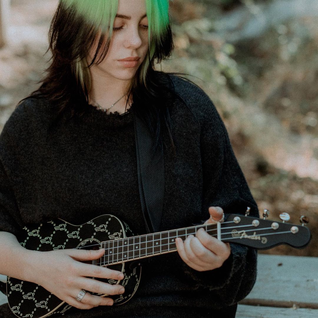 Billie Eilish looks down as she strums on a Fender ukulele. 