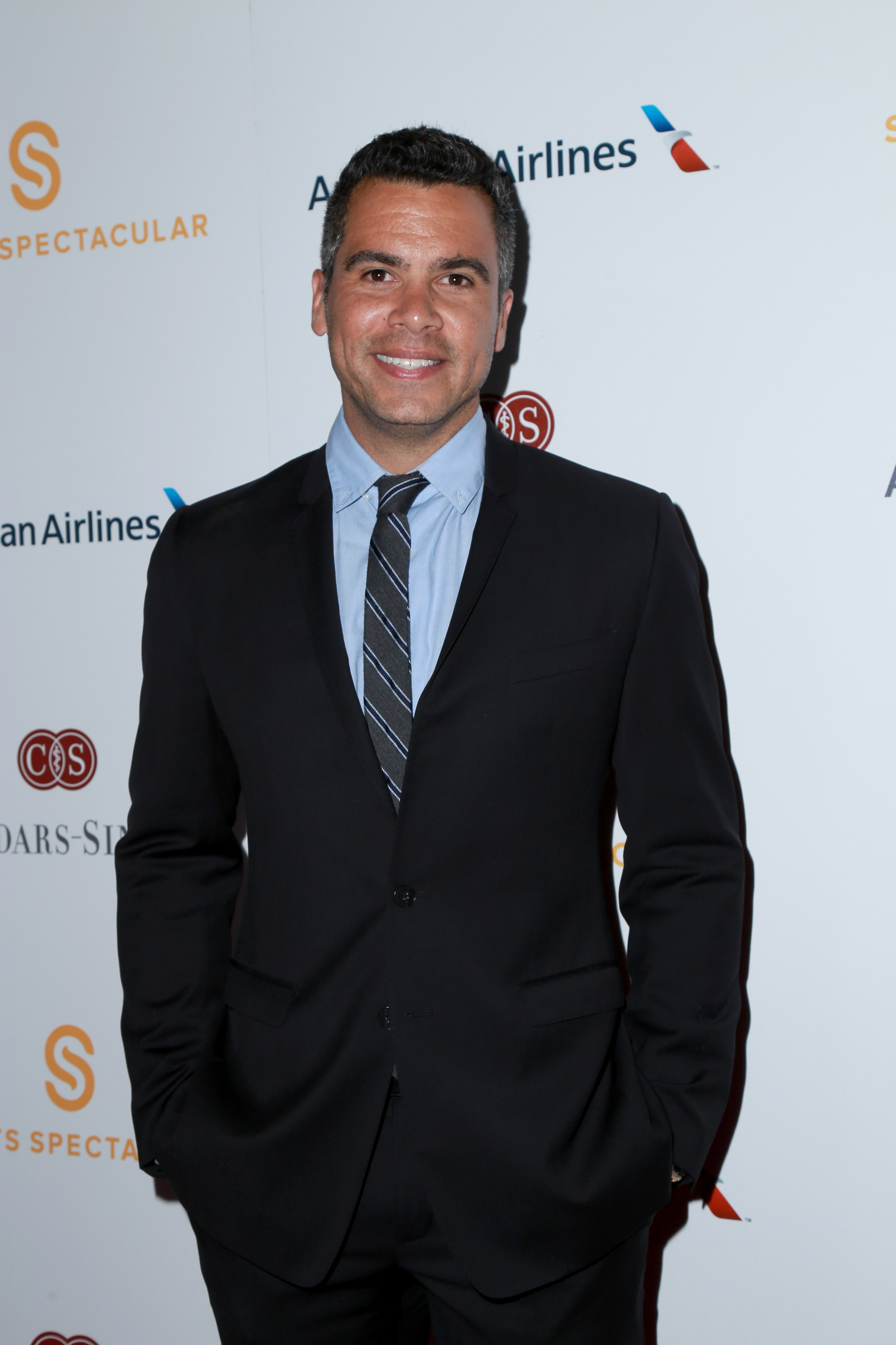 A photo showing Cash Warren in a well-fitted black suit and pant, paired with a gray striped tie and blue inner T-shirt.