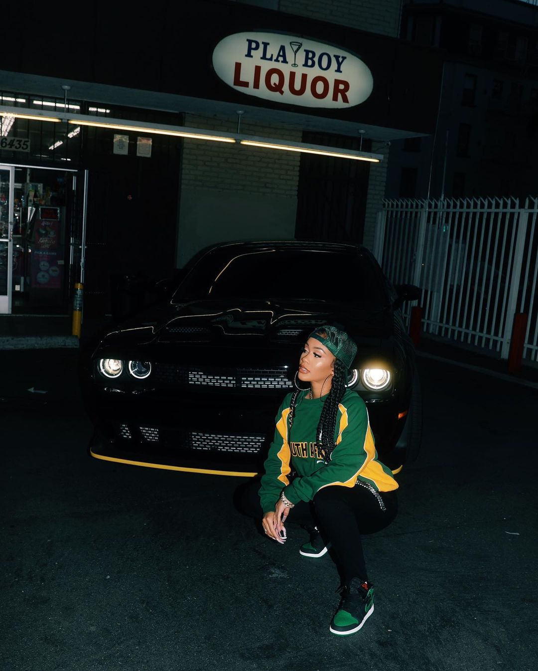 A photo showing Saweetie in a green and yellow design sweatshirt with a matching cap and sneakers and black pant.