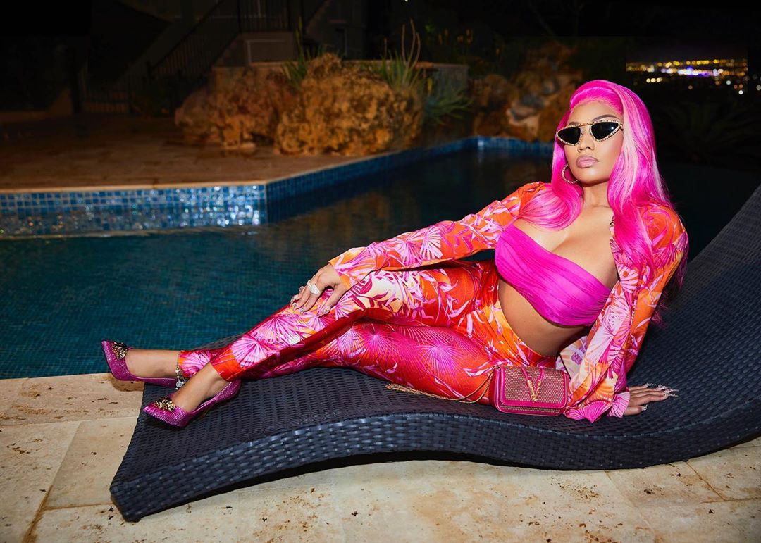 A photo showing Nicki Minaj in an all-pink outfit and accessories, sitting by a pool.