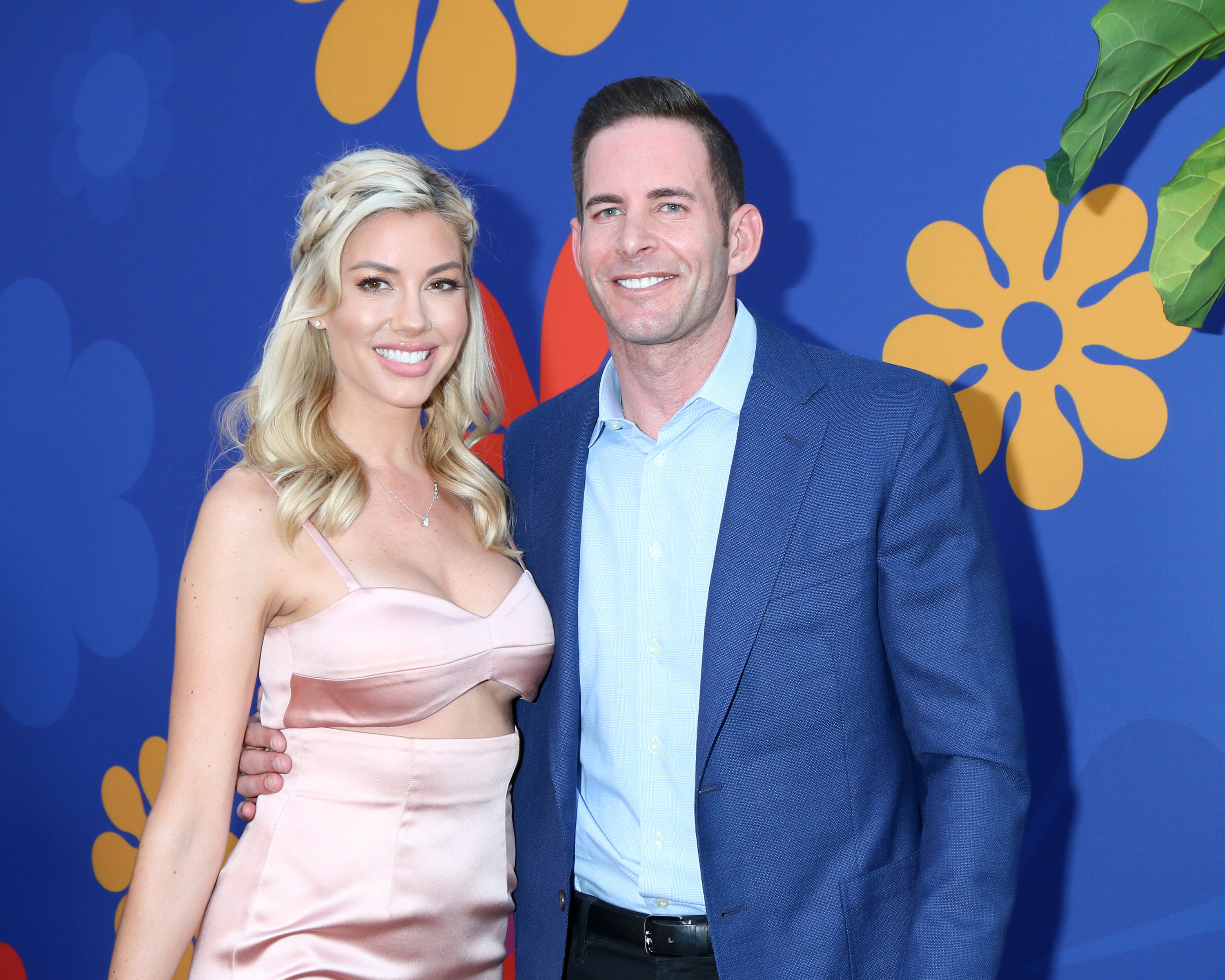 A photo showing Tarek El Moussa in a blue suit and black pant, beside Christina Haack, who has on a peach color bralette and skirt.