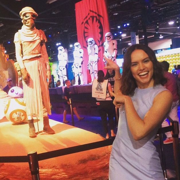 Daisy Ridley points at a Rey costume and smiles. 